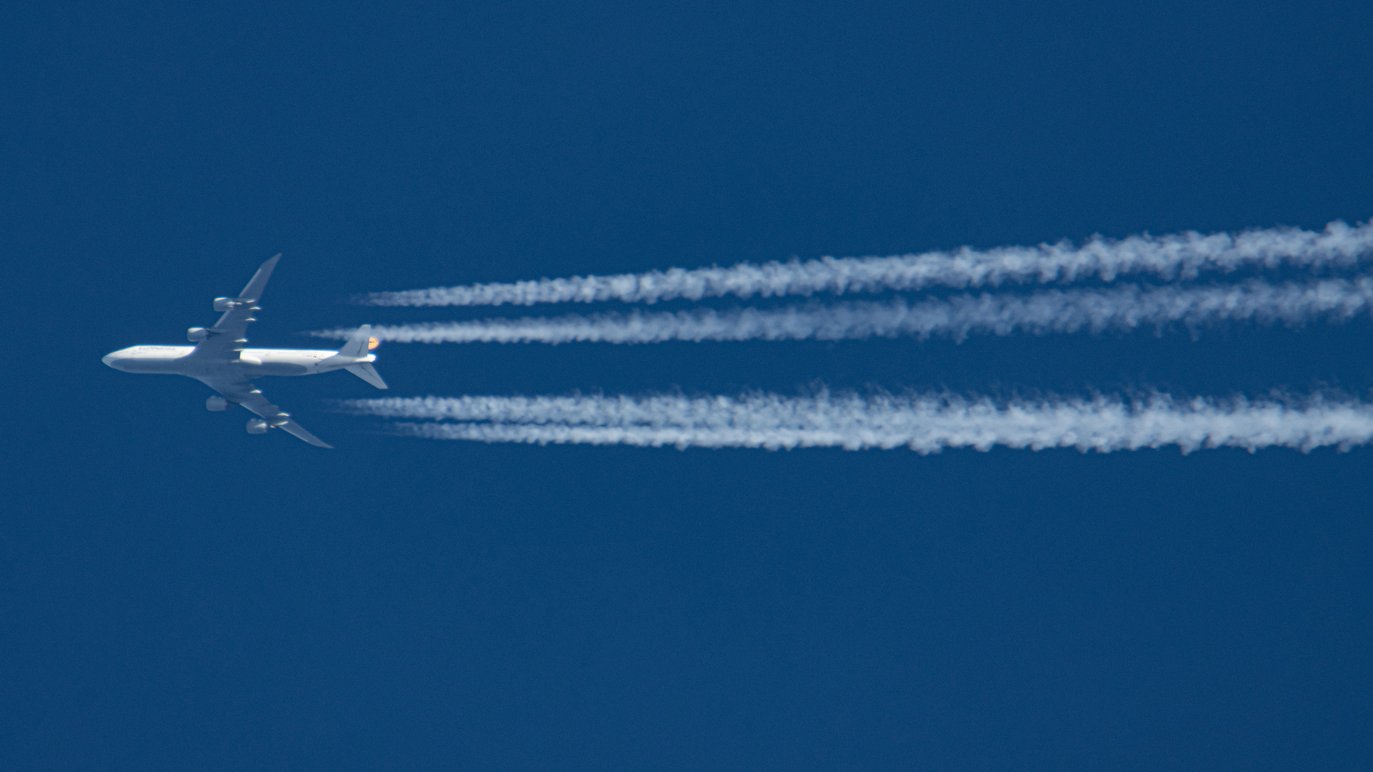 A Lufthansa Boeing 747-8 aircraft spotted flying from Frankfurt FRA airport in Germany to Chicago. The overflying jumbo jet airplane is leaving behind contrails or condensation trail, a white vapor line.