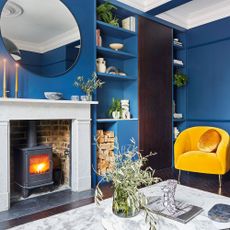 living room with blue wall yellow chair round mirror and fire place