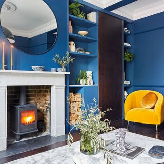 living room with blue wall yellow chair round mirror and fire place