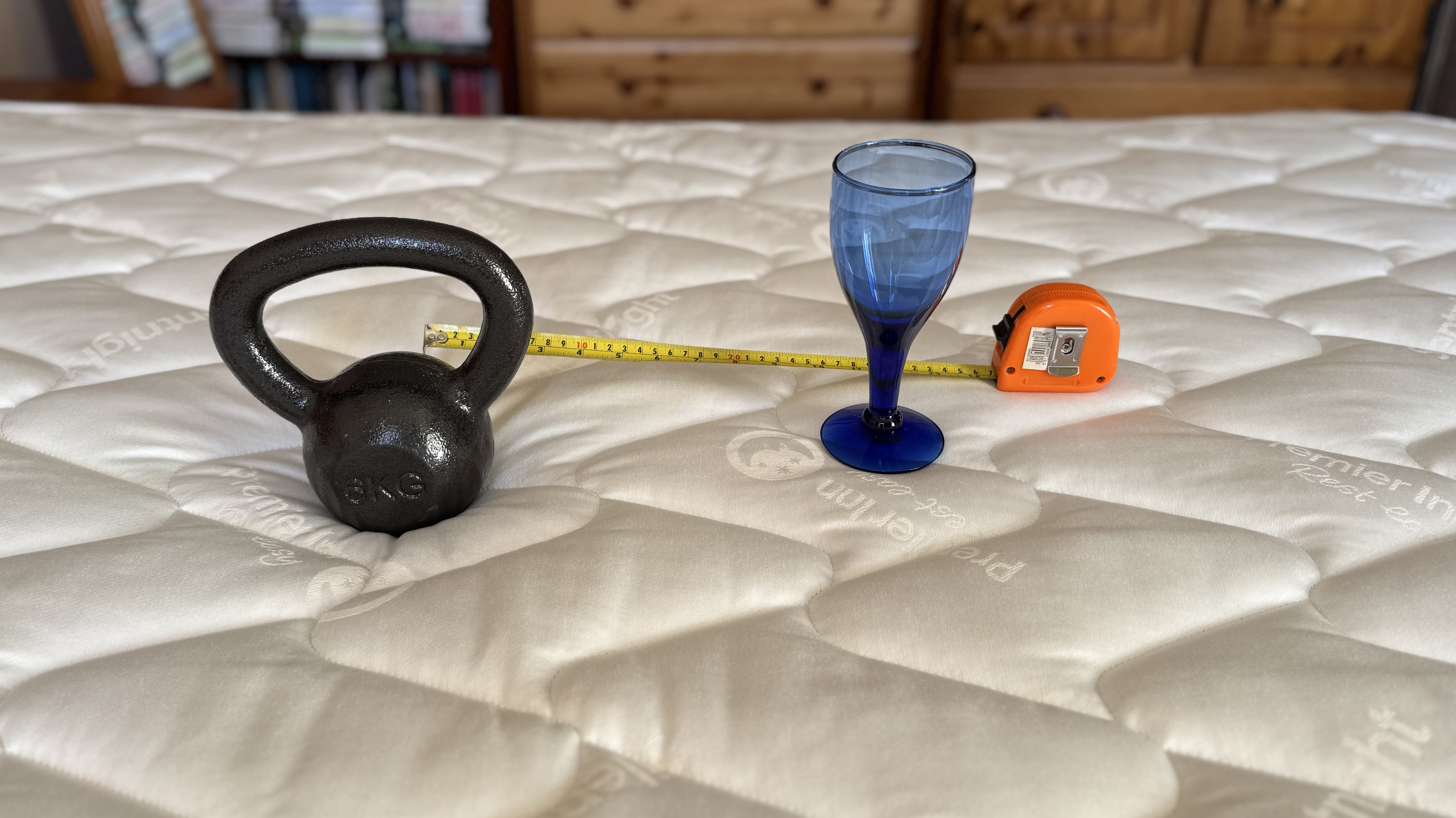 A small weight, wine glass and tape measure set up to measure motion isolation on a mattress.