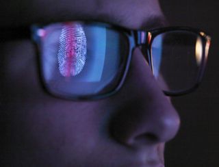 A close up of a face wearing glasses, with a reflection of digital information and a fingerprint reflected in the lenses