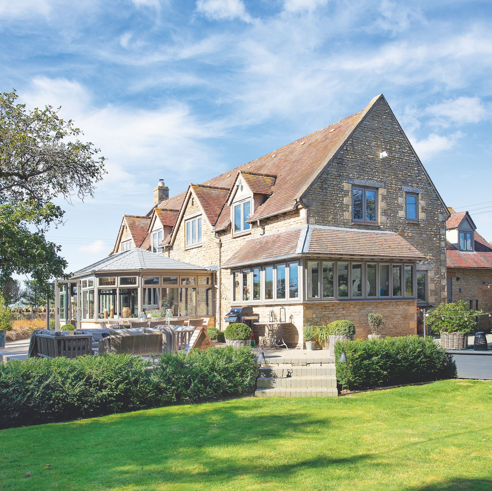 exterior of large cotswold stone house with garden room and large green lawn
