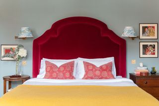 bright red headboard and yellow covers with red pillows and pale green walls with bright artwork and wall lamps with blue shades