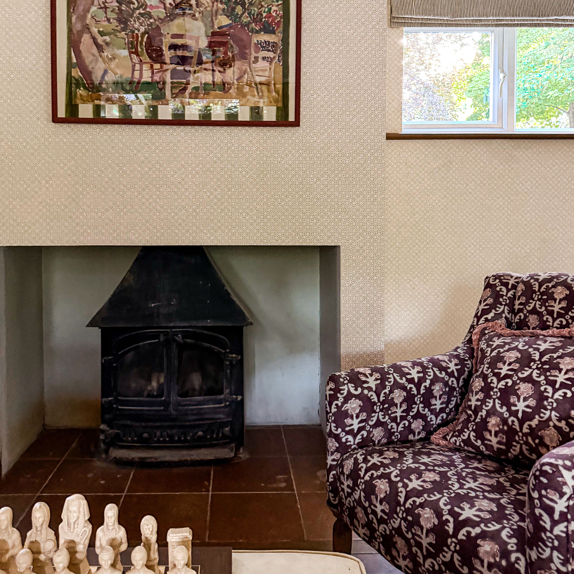 Patterned armchair with matching cushion beside log burner inset into wall