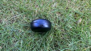 The motorola moto buds 150 pictured in their charging case on grass.