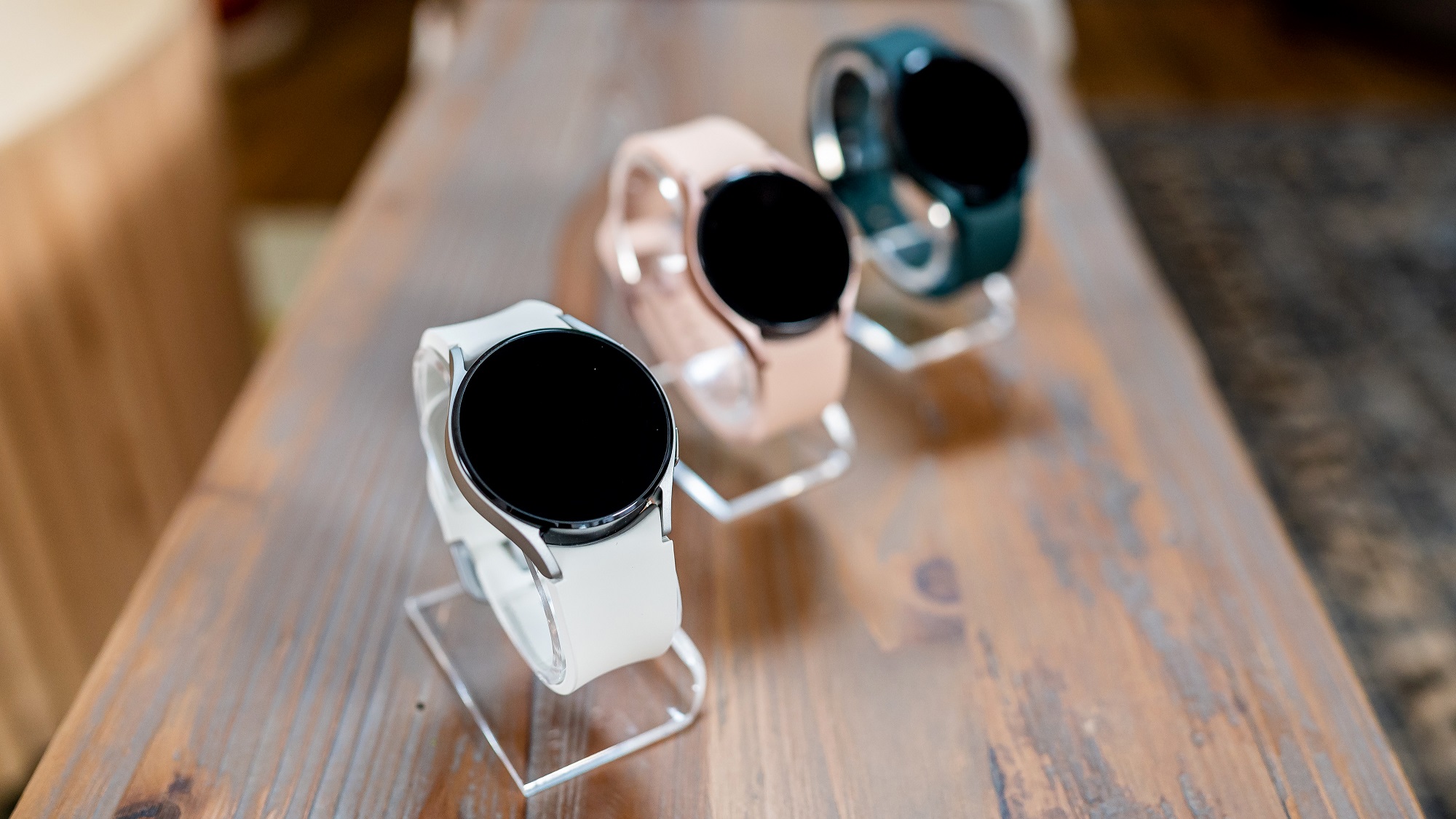 Línea de tres relojes inteligentes Samsung Galaxy Watch 4 sobre mesa de madera en el evento de lanzamiento Galaxy Unpacked.