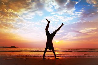 A man does a cartwheel on a beach at sunset.