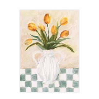 A watercolor wall art print with yellow tulip flowers in a white curved vase, a beige backdrop on a white and green checked table