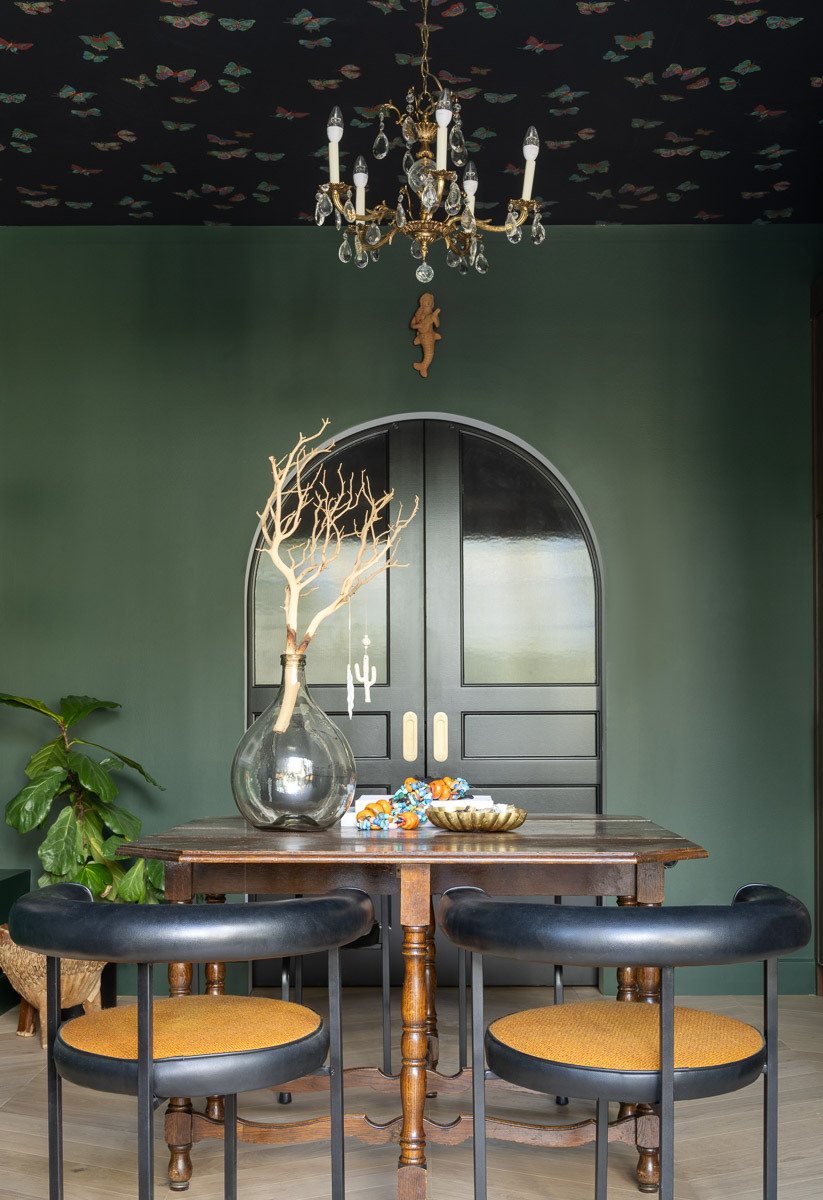 Green-painted office space with a black wallpapered ceiling and black accents. On the desk is a vase with a decorative branch inside.