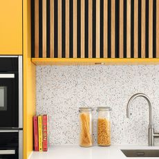 Yellow painted kitchen with wood panelling feature and white terrazzo tiles