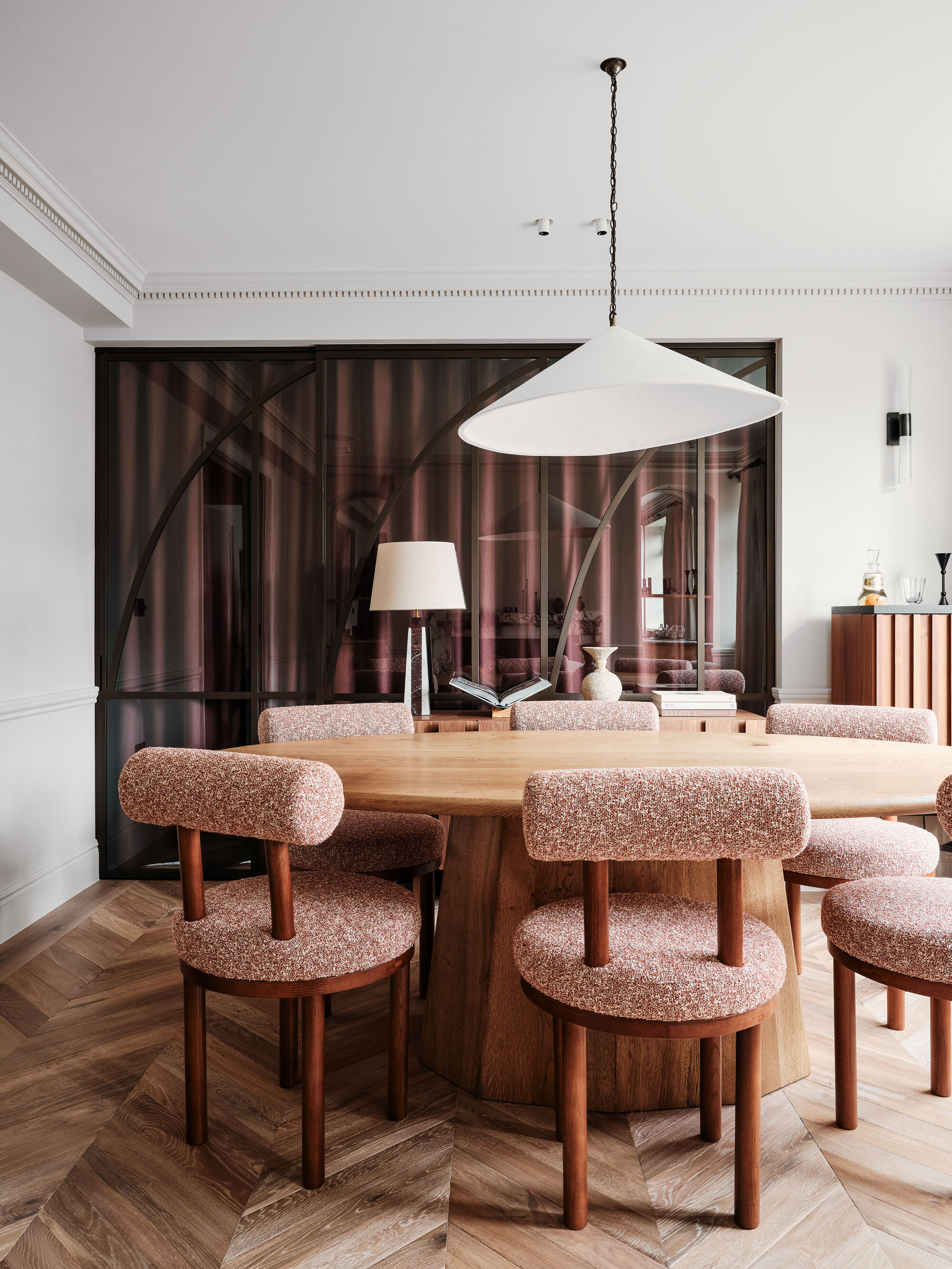 A round wooden dining table with red chairs and a hanging white pendant feature light