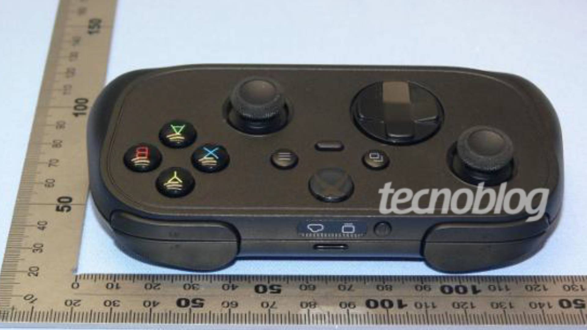 Black Xbox compact controller next to square ruler sitting on blue surface.