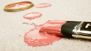A paintbrush with pink paint which has spilled on the carpet