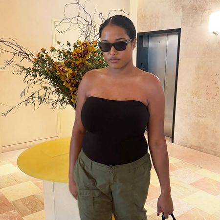 a woman wearing a black tube top, green cargo pants, black sandals, and black sunglasses