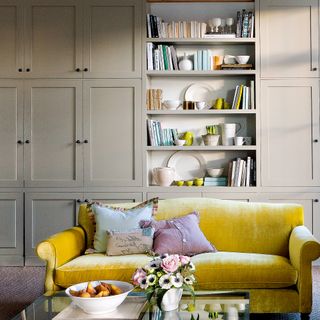 A living room with built-in closed storage and a yellow 2-seater sofa