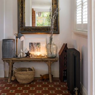 Wooden table topped with a lamp, lit candles and accessories on top of a patterned floor with a wall-mounted mirror