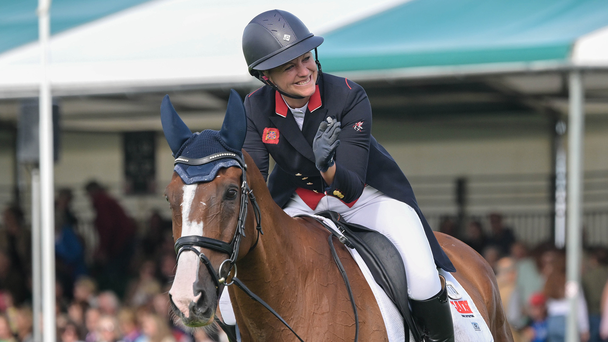Gemma Stevens, a rider in a blue tailcoat with red trim, smiles and pats her chestnut horse, Chilli Knight, after her Burghley dressage test