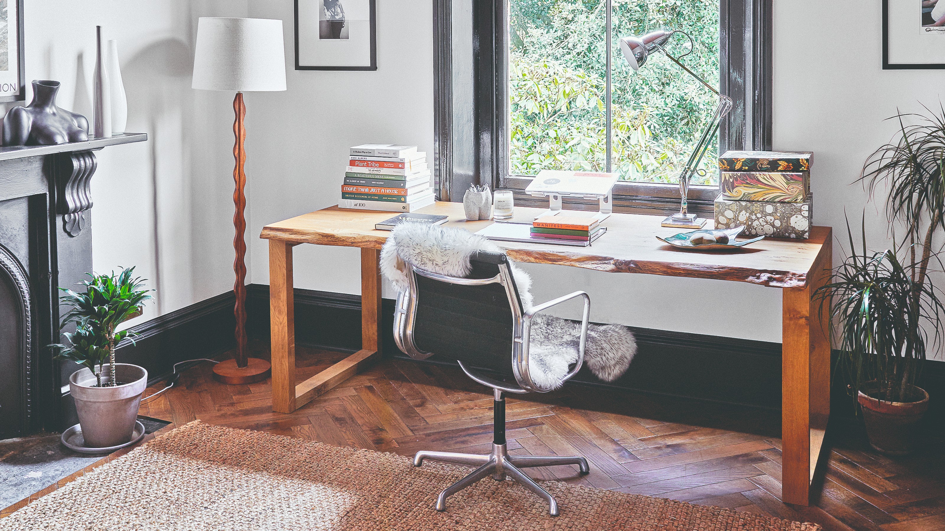 A big home office with a wooden desk and wiggly floor lamp with a monitor stand on the desk