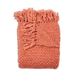 A folded coral chunky knit throw blanket with tasseled detailing