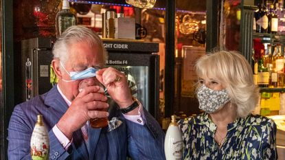 Camilla Parker Bowles showed off her witty side during a recent pub visit with Prince Charles. CLAPHAM, ENGLAND - MAY 27: Prince Charles, Prince of Wales adjusts his face mask to enable him to sip a pint that he pulled in a pub alongside Camilla, Duchess of Cornwall during a visit to Clapham Old Town on May 27, 2021 in Clapham, England. (Photo by Heathcliff O&#039;Malley - WPA Pool/Getty Images)