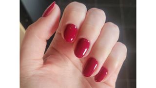 A close up of Digital Beauty Writer, Naomi Jamieson's red almond nails/ in front of a grey background