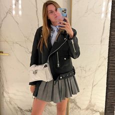 French writer and editor Eugenie Trochu posing for a mirror selfie wearing a black leather moto biker jacket with a gray pleated skirt