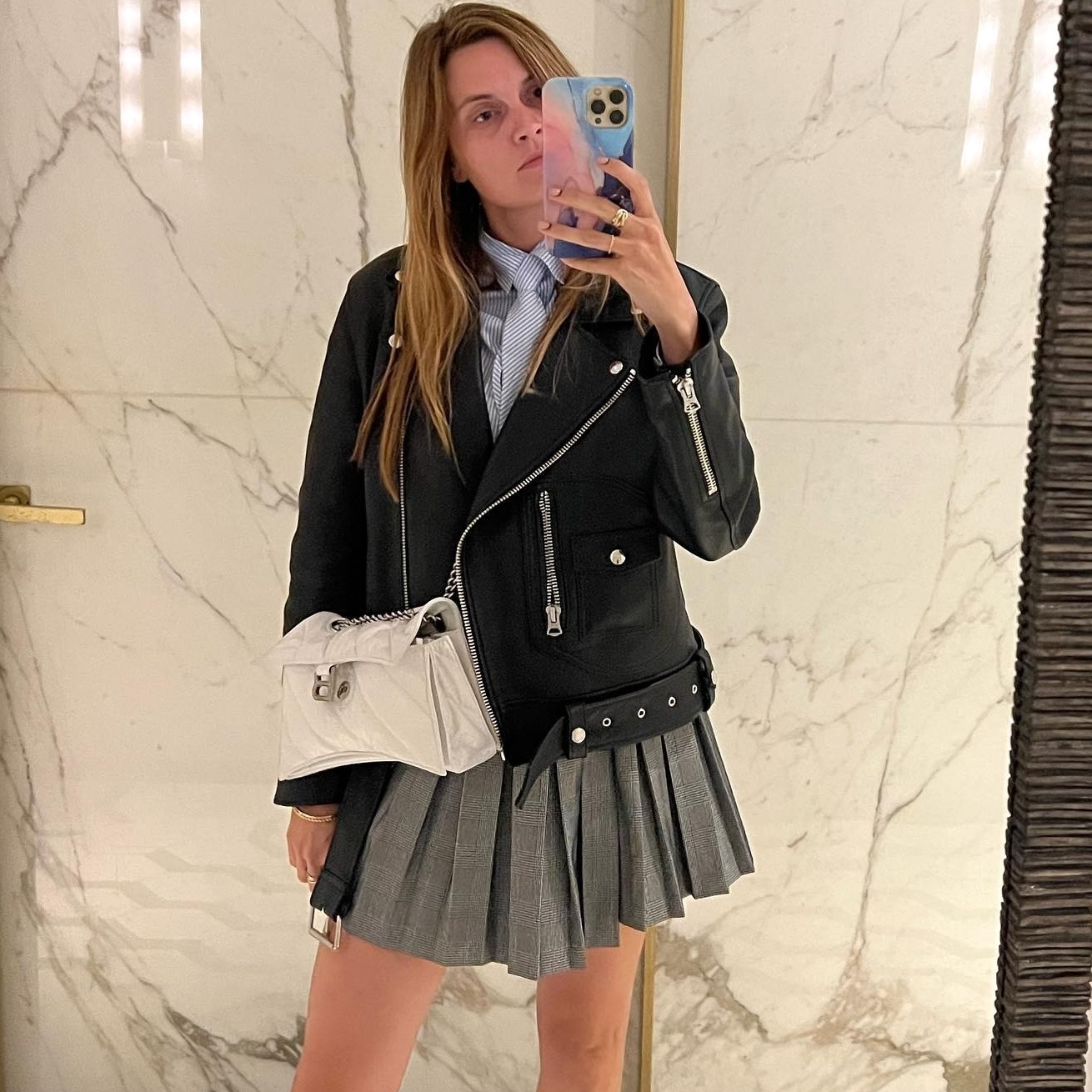 French writer and editor Eugenie Trochu posing for a mirror selfie wearing a black leather moto biker jacket with a gray pleated skirt
