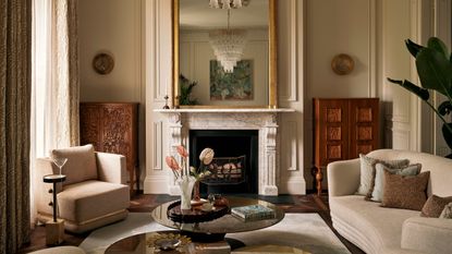 Elegant living room with neutral walls, a stone marble fireplace with a gold mirror above and wooden cabinets in the alcoves