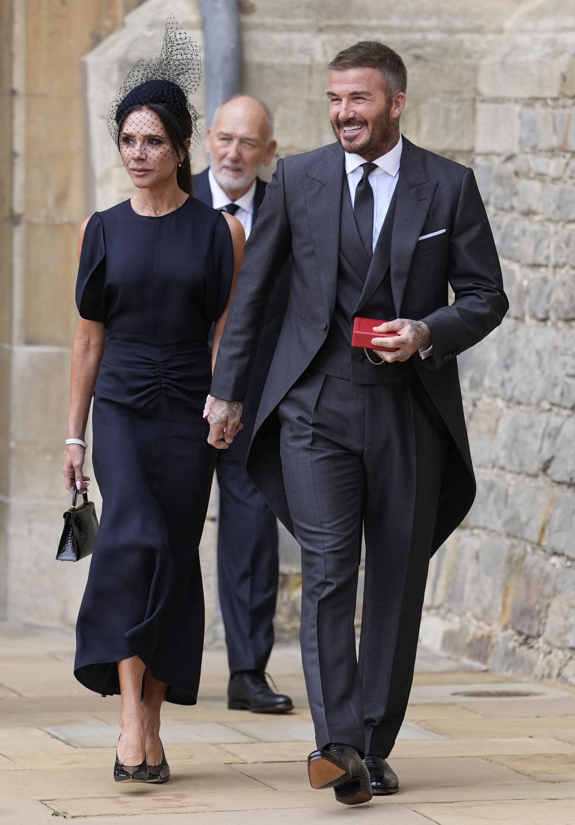 Victoria Beckham walks hand-in-hand with David Beckham, wearing a navy dress with black croc-print heels and a black croc bag.