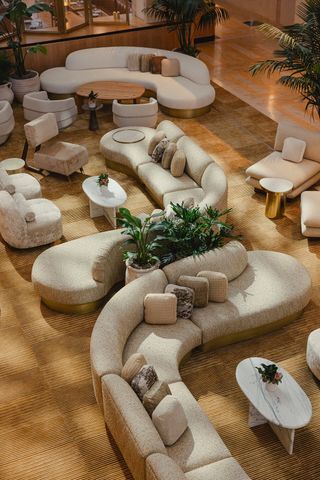 1970s-inspired, large-scale sofas in creme serve as the centerpiece of a hotel hall filled with neutral-colored furniture and plants.