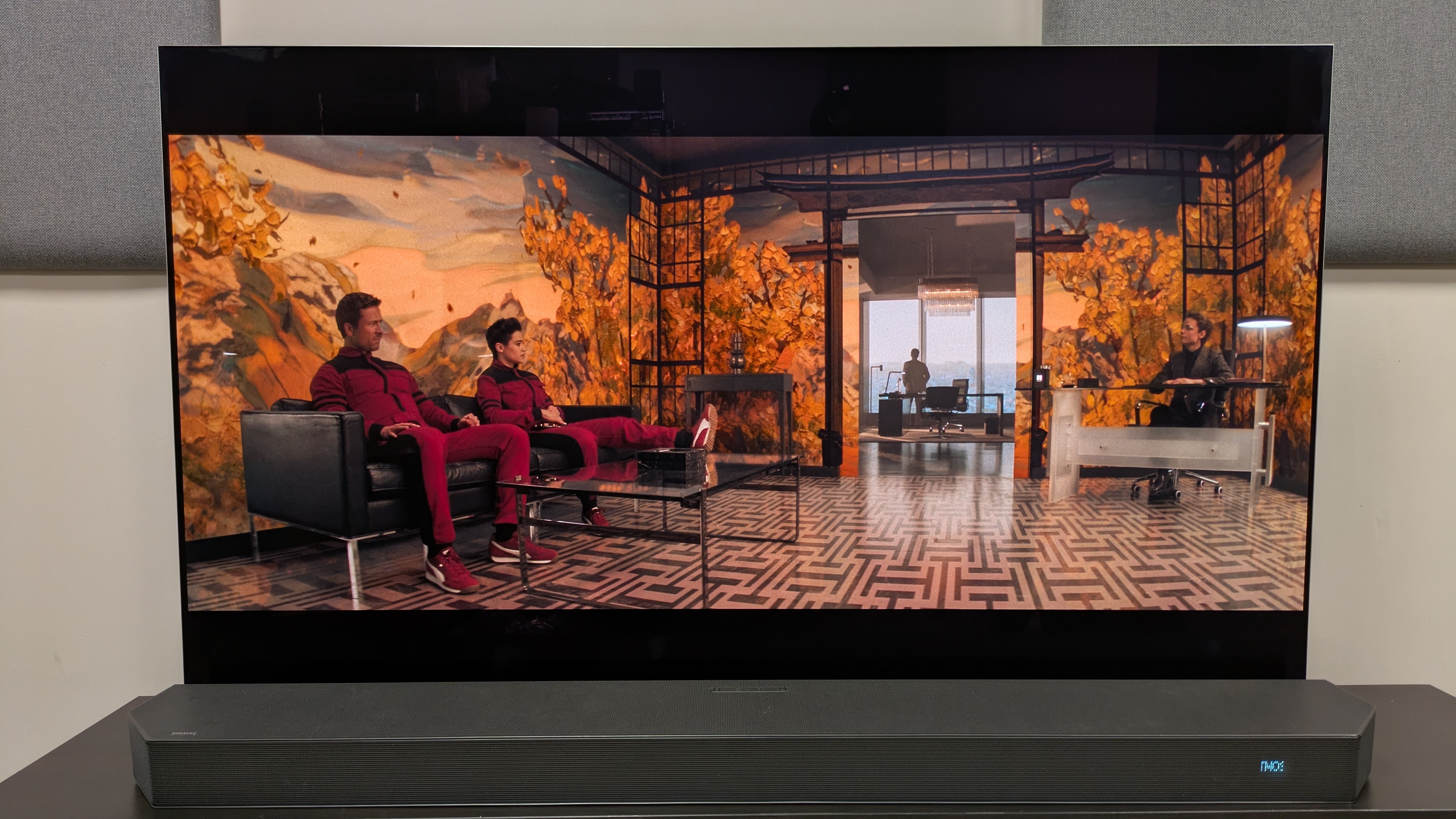 The Running Man (2025) 4K Blu-ray on LG G5 OLED, showing Ben and Jenni sat in a waiting area with a floral pattern on the walls 