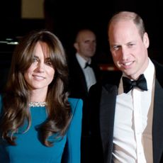 Kate Middleton wears a teal dress and has long brunette hair and bangs, Prince William wears a tuxedo