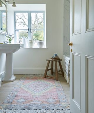 pastel toned rug with white tassels in white bathroom with sink and wooden stool
