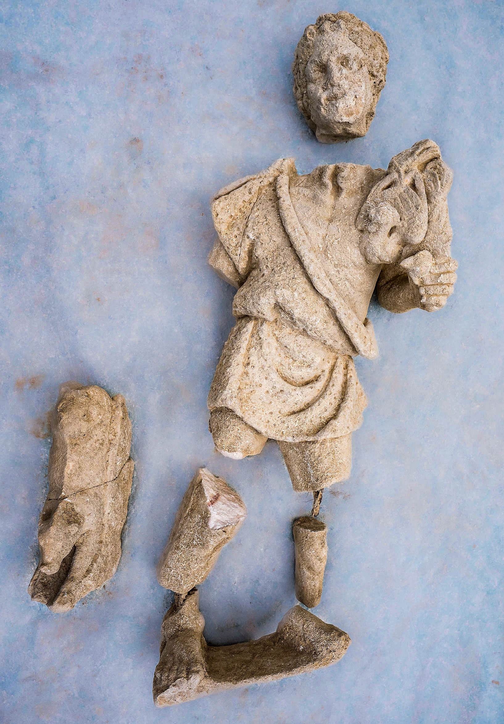 a fragmented marble sculpture of an ancient Roman deity (Silvanus) lies on a blue table