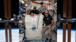 an image of four astronauts in costumes at the front. the background shows a blurry image of the international space station
