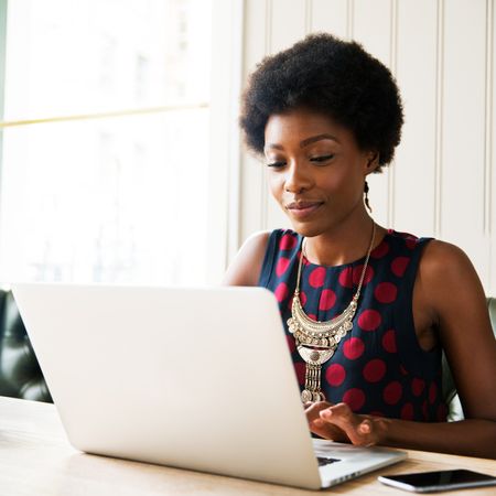 A woman grinning while reading her laptop.
