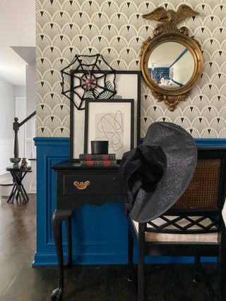 An entryway with a credenza decorated for Halloween with a witches hat, a faux spider web, and a stack of books