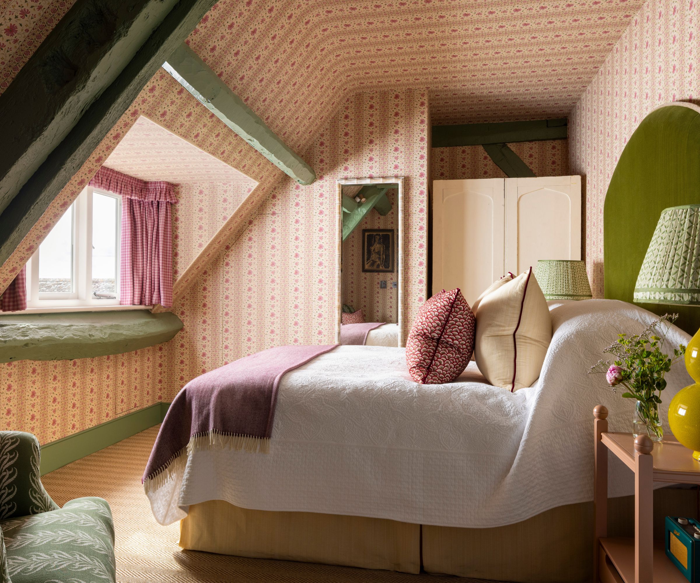 pink floral wallpapered bedroom with sloped ceilings and a bed with a green velvet headboard