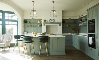 Sage green kitchen with a kitchen island, marble worktops and pendant lights