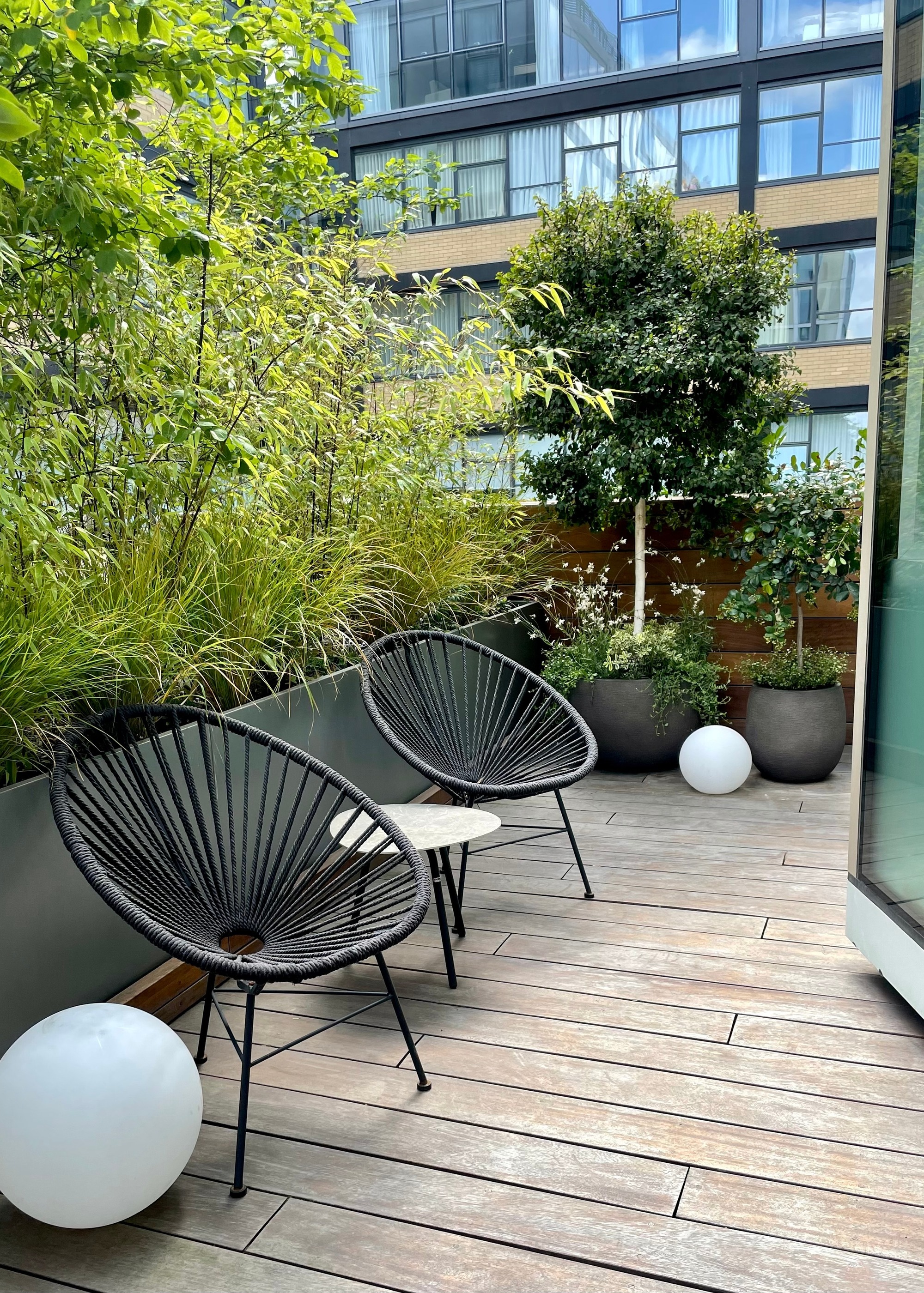 Apartment balcony with timber deck and tall potted plants for shade and privacy