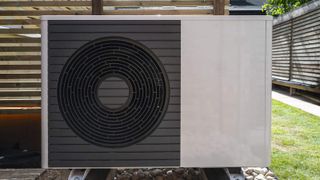 Front view of the air source heat pump outside in the garden, near wooden fence on a sunny day