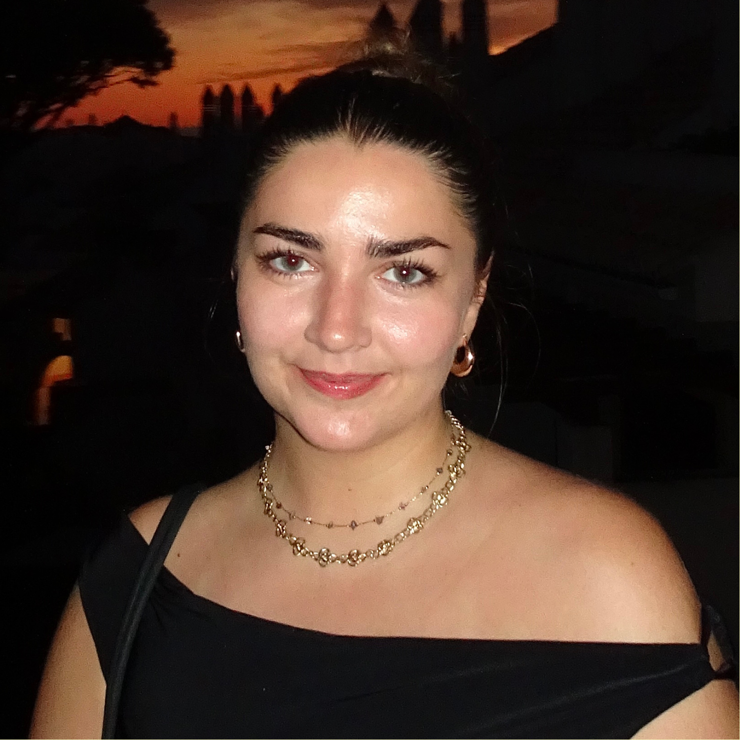 A woman with slick back hair and gold jewellery in a black off-shoulder top