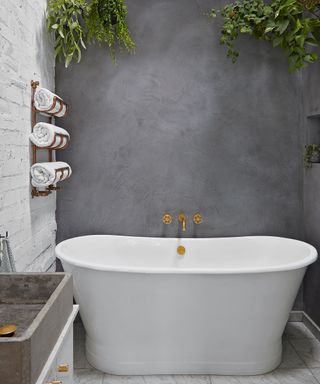 A modern bathroom with a concrete wall and small white free-standing bathtub