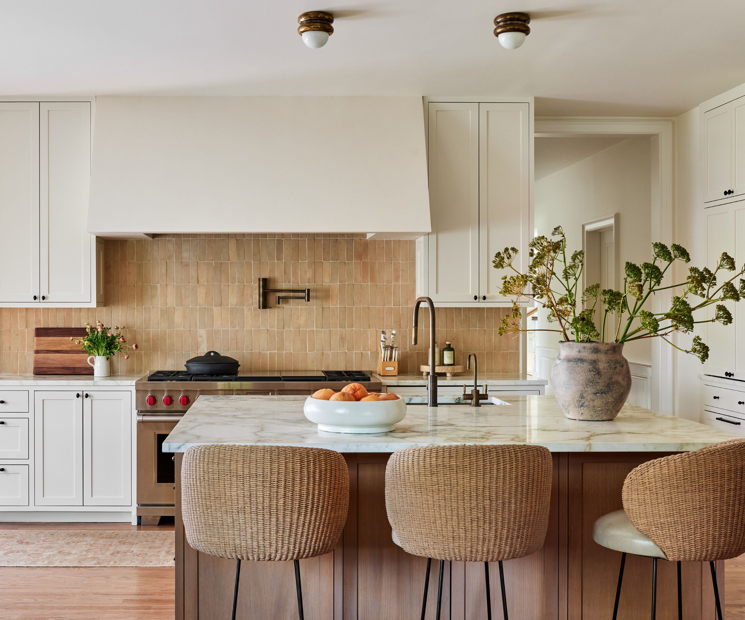 Kitchen with brown zeillage tiles, marble island, rattan bar stools and rustic vase with stems