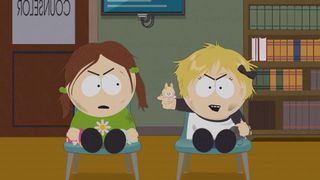 Two girls sat on chairs next to each other with the blonde girl on the right holding up a Labubu doll