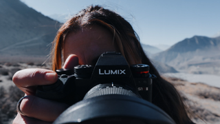 A person holds the LUMIX S1RII, framed against a stunning mountainous landscape with clear skies