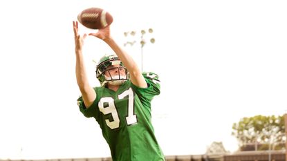 A football player with the number 97 on his jersey catches a football.
