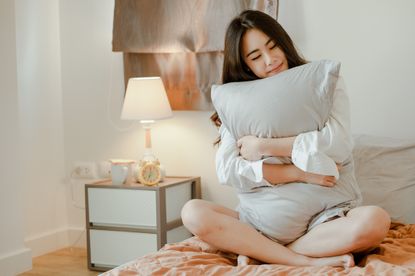 Young Woman Embracing Pillow While Sitting On Bed At Home - Best pillows for sleep