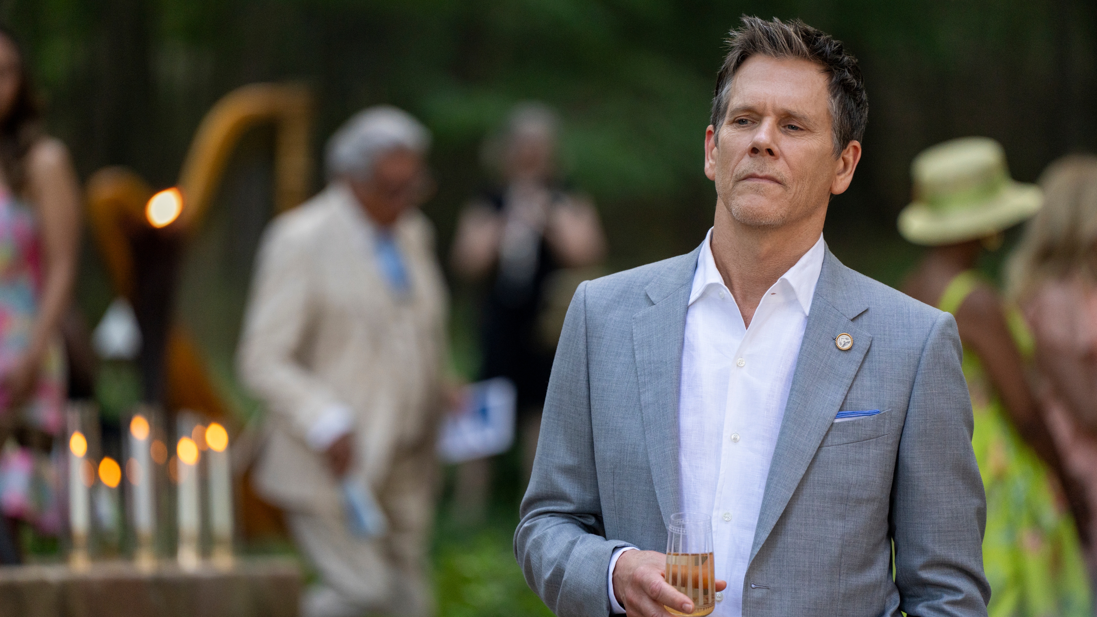 Kevin Bacon as Peter Kell in a suit and drinking champagne