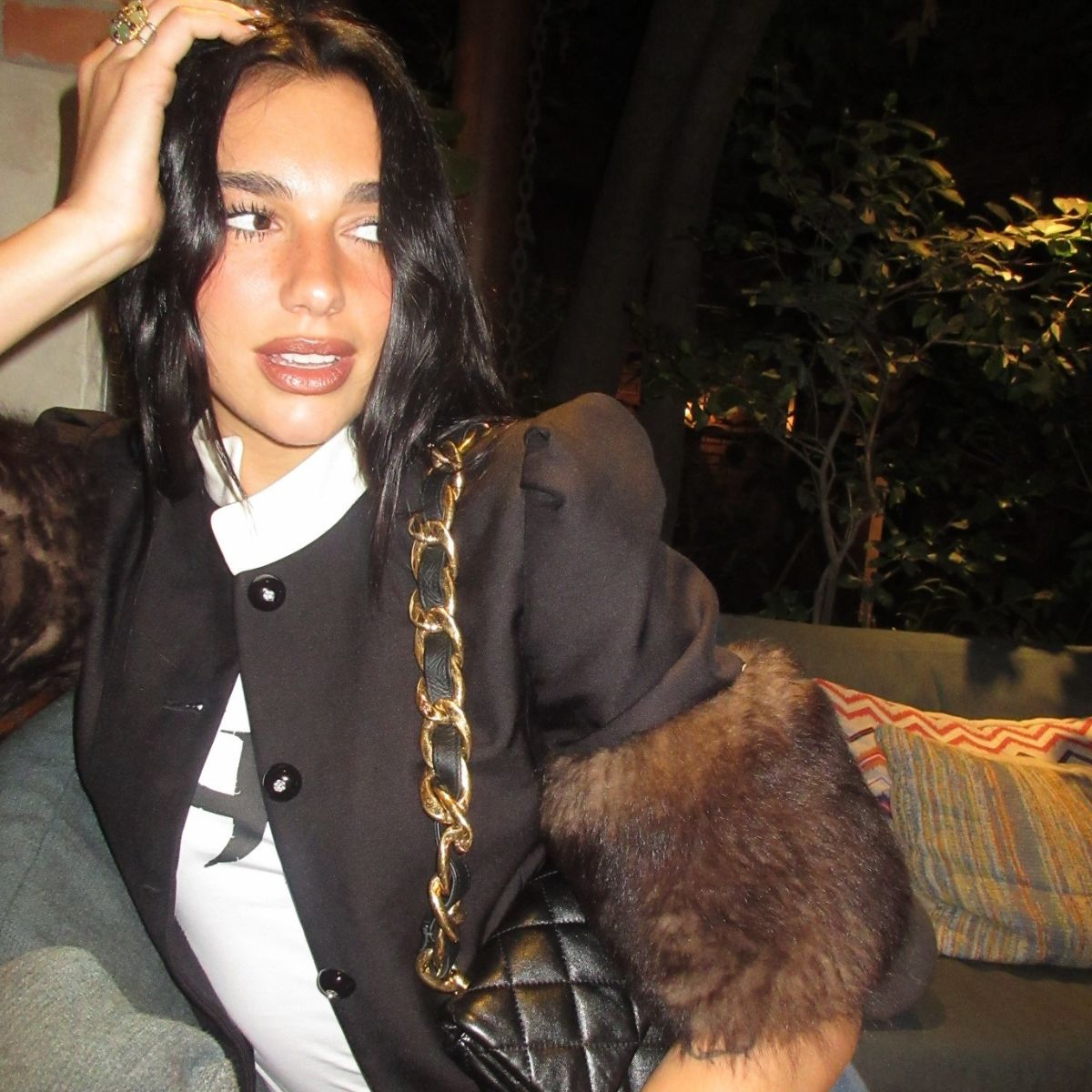 Dua lipa posing with her hand on her head wearing a faux fur trimmed jacket